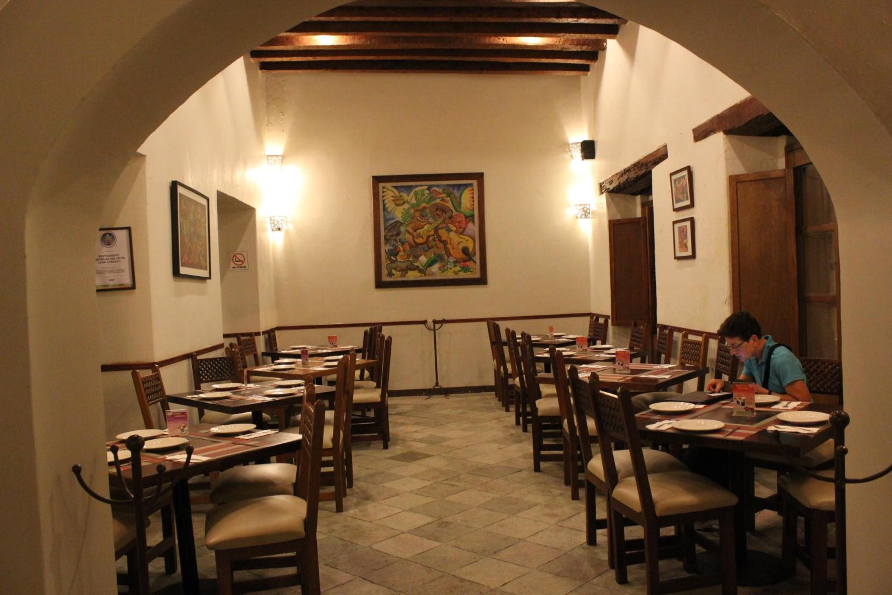 A dining area with multiple tables and chairs, a central painting, and a person seated at a table.