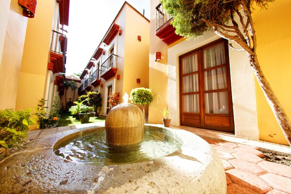 A courtyard with a fountain, potted plants, and a building with a large window and door. - Hotel Casa Conzatti (Oaxaca)