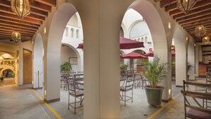 An indoor courtyard with arches, potted plants, and wooden furniture.