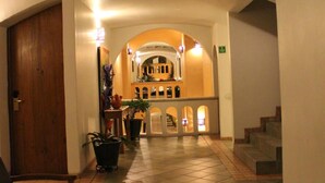 A hotel lobby with a tiled floor, wooden chairs, a small table, and a staircase leading to an upper level.