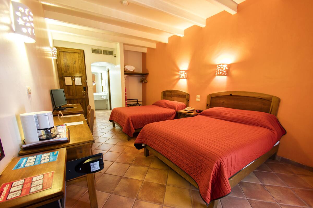 A hotel room with two beds, a desk with a computer, and a chair.