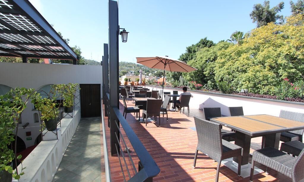 Une terrasse extérieure aménagée avec des meubles en osier, une table et des chaises. Un grand parasol offre de l’ombre.