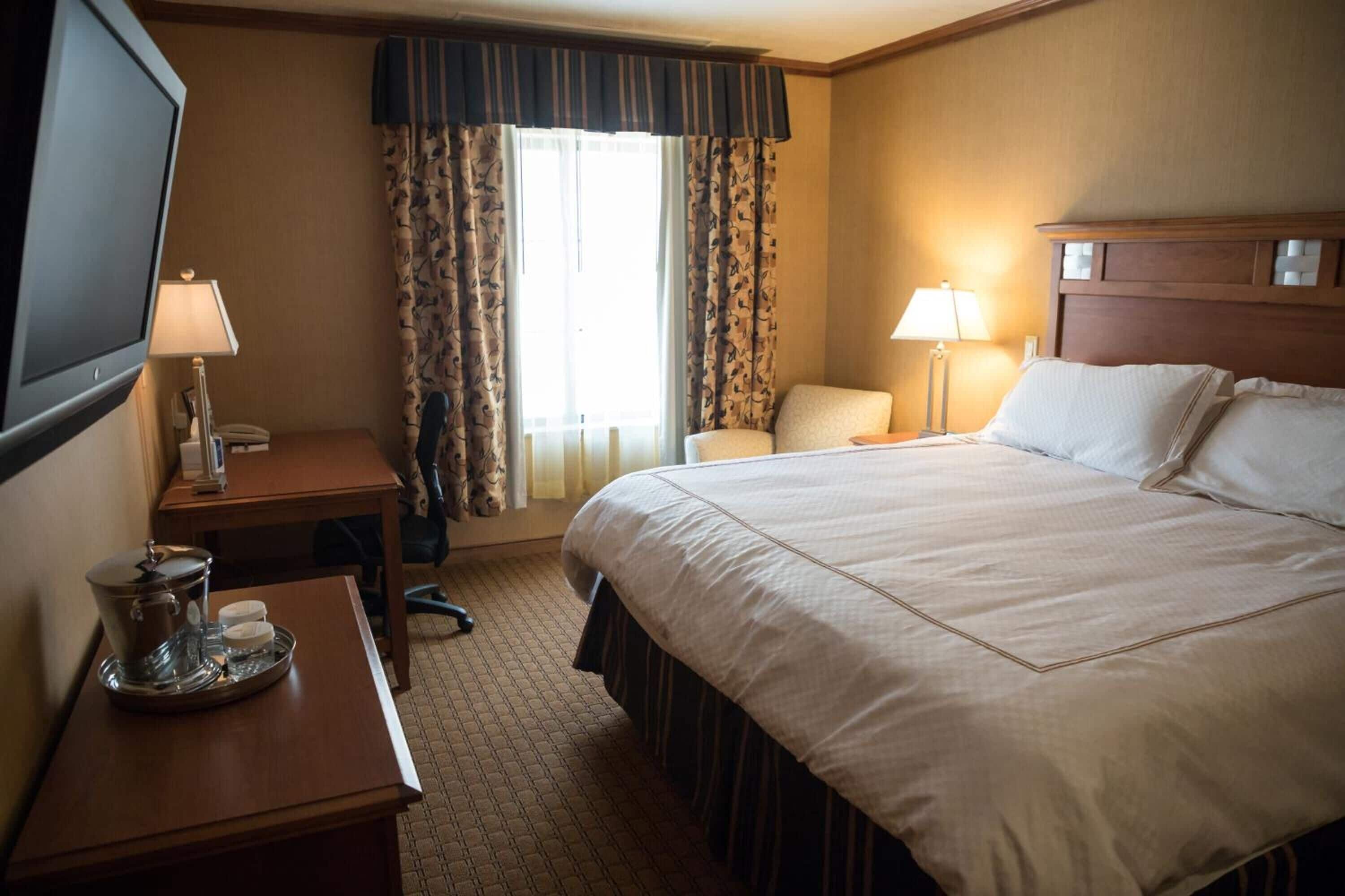 A hotel room with a large bed, a desk with a lamp, a chair, and a television.