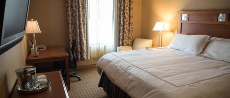 A hotel room with a large bed, a desk with a lamp, a chair, and a television.