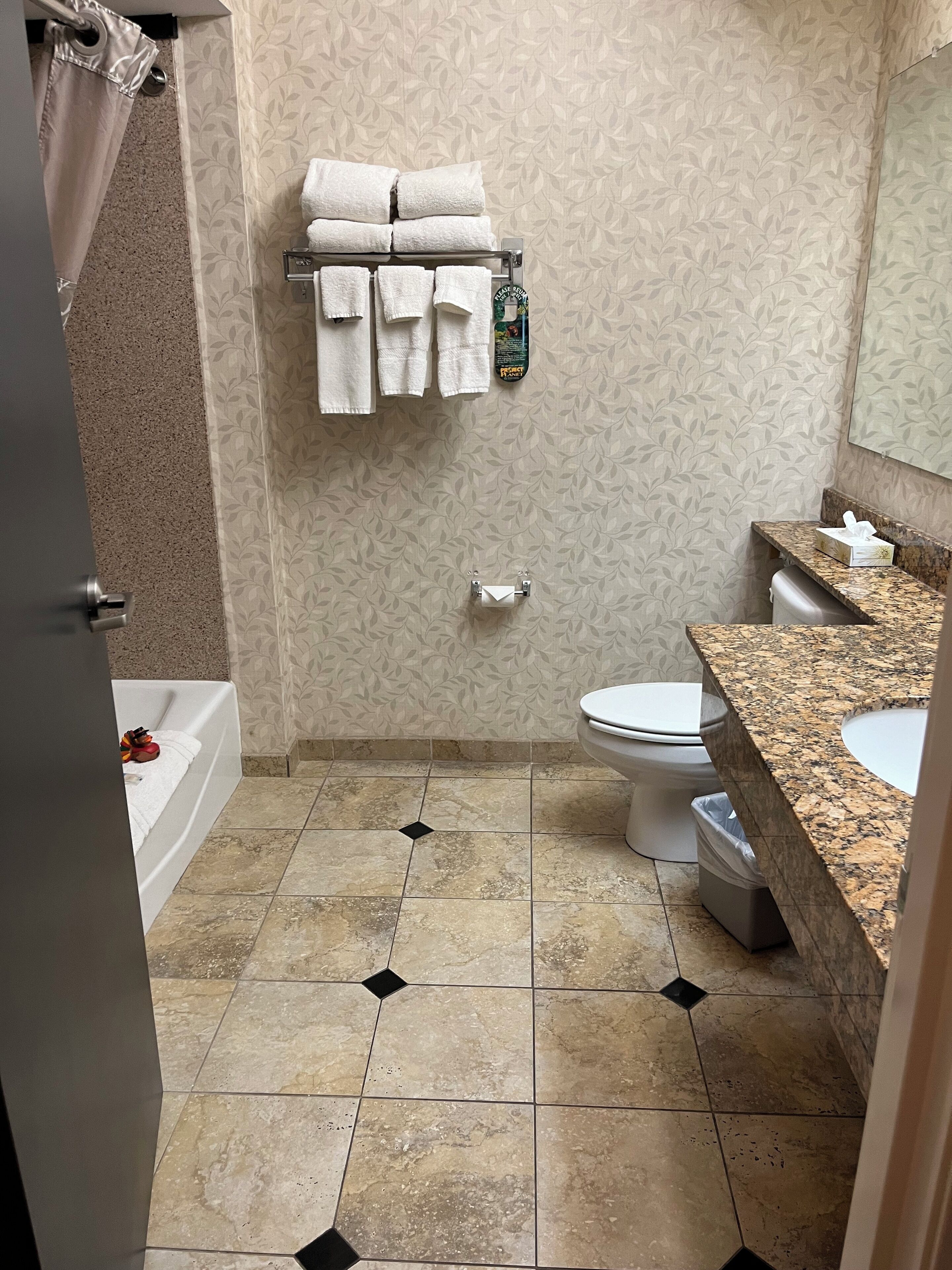 Une salle de bain avec une baignoire, des toilettes et un lavabo. Des serviettes sont suspendues sur un porte-serviettes et il y a une poubelle.