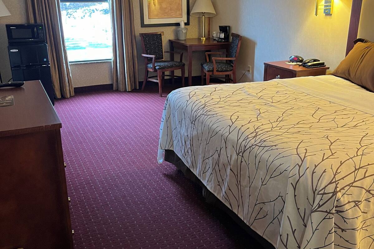 A hotel room with a large bed, a desk with two chairs, a microwave, a telephone, and a window with curtains.