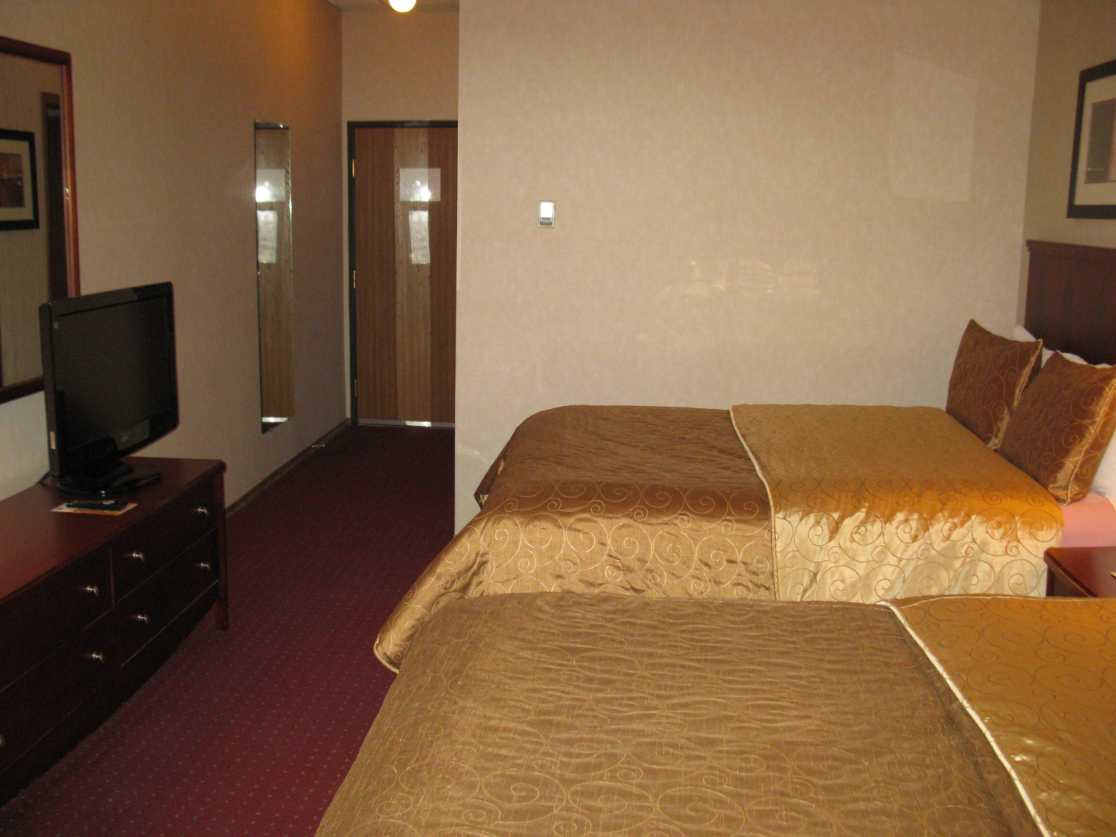 Une chambre d’hôtel avec un lit, un téléviseur posé sur une commode et une porte donnant sur une autre pièce.