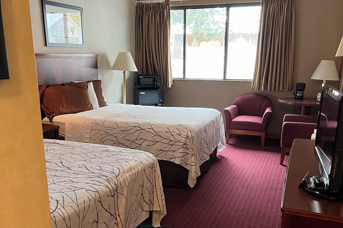 A hotel room with two beds, a desk with a computer, a chair, a window with curtains, and a framed picture on the wall.