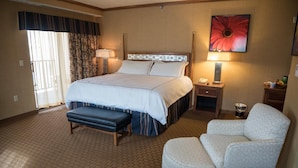 A hotel room with a large bed, a bench, a chair, a bedside table, a lamp, and a painting on the wall. - Mineral Palace Hotel & Casino (Deadwood)