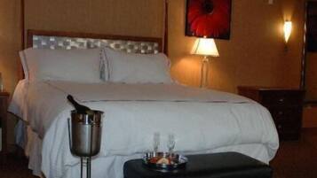A hotel room with a bed, a nightstand, a lamp, a bucket, and a tray with glasses and a bottle.