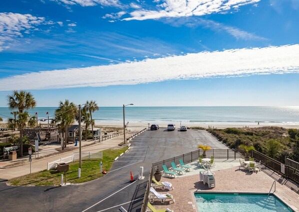 A beachfront hotel with a pool, lounge chairs, and a view of the ocean.
