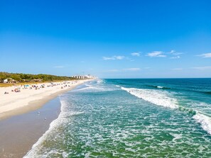 A beach with a clear sky, waves, and a distant cityscape.
