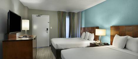 A hotel room with two beds, a desk with a TV, a lamp, and a door.
