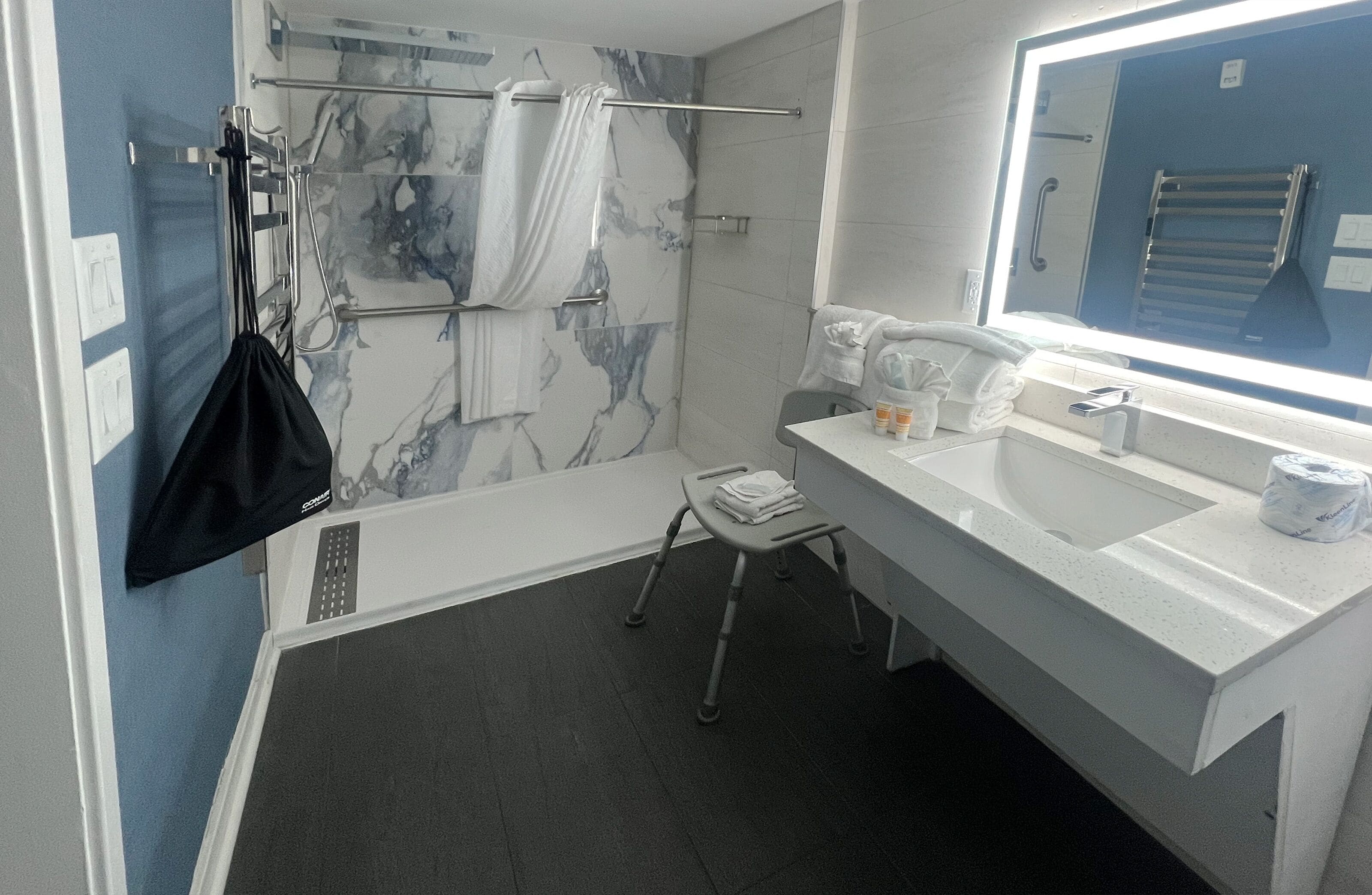 A modern bathroom with a marble shower wall, a white sink, and a large mirror.