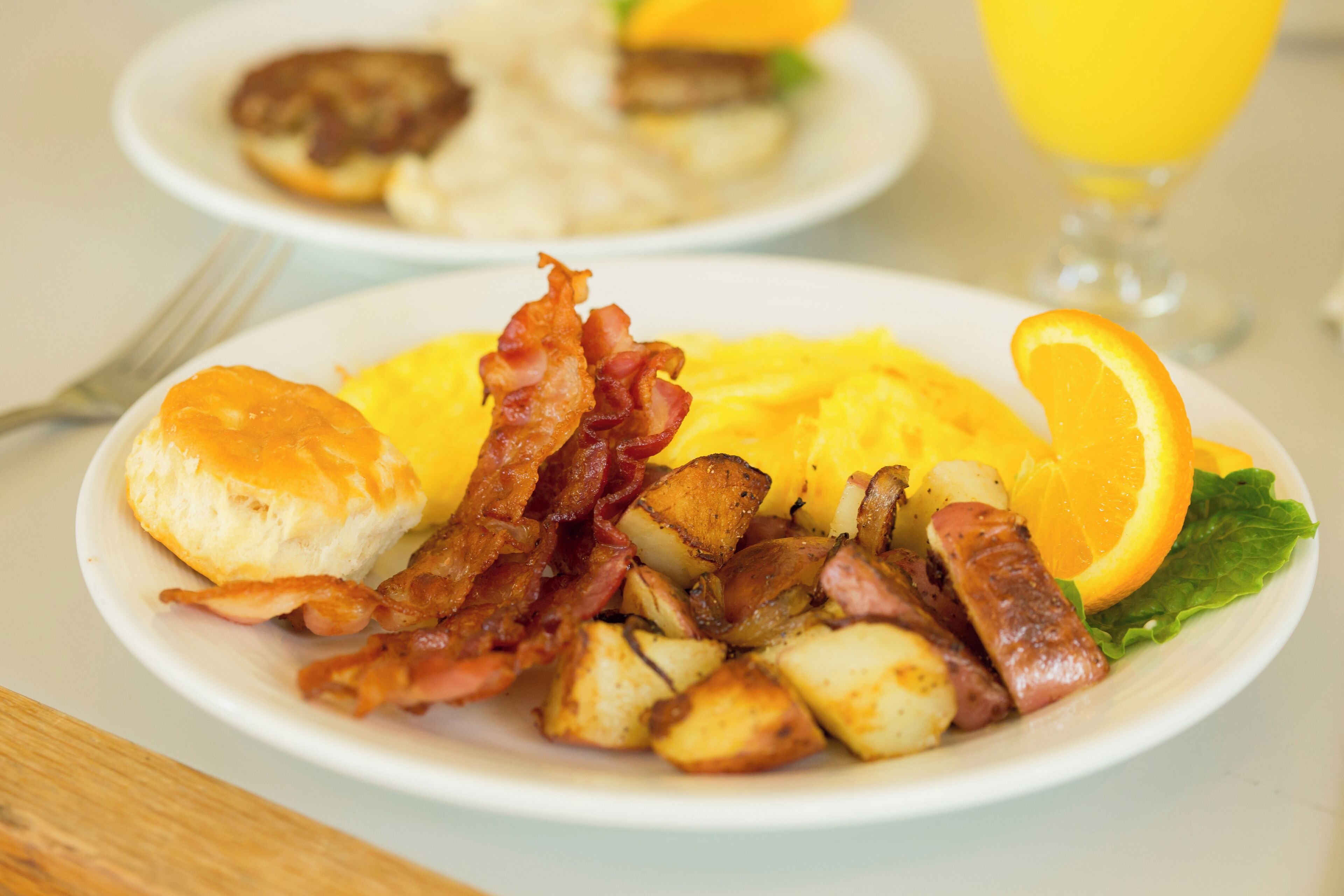 Un piatto da colazione con bacon, uova, patate e una fetta d'arancia.
