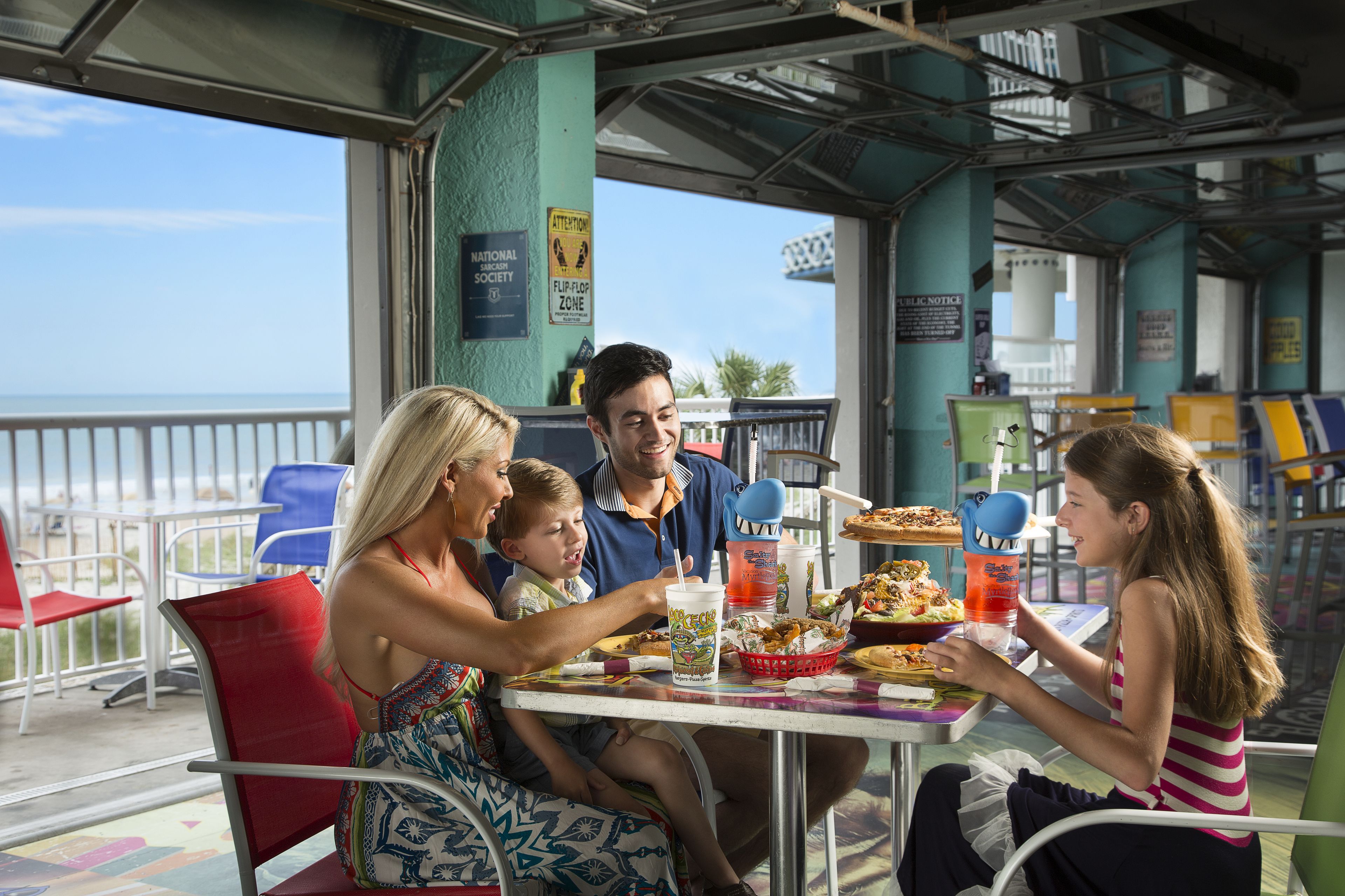 Une famille prend son repas dans un restaurant en plein air, avec vue sur l’océan.