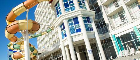 Un hotel con tobogán acuático, piscina y varios balcones.