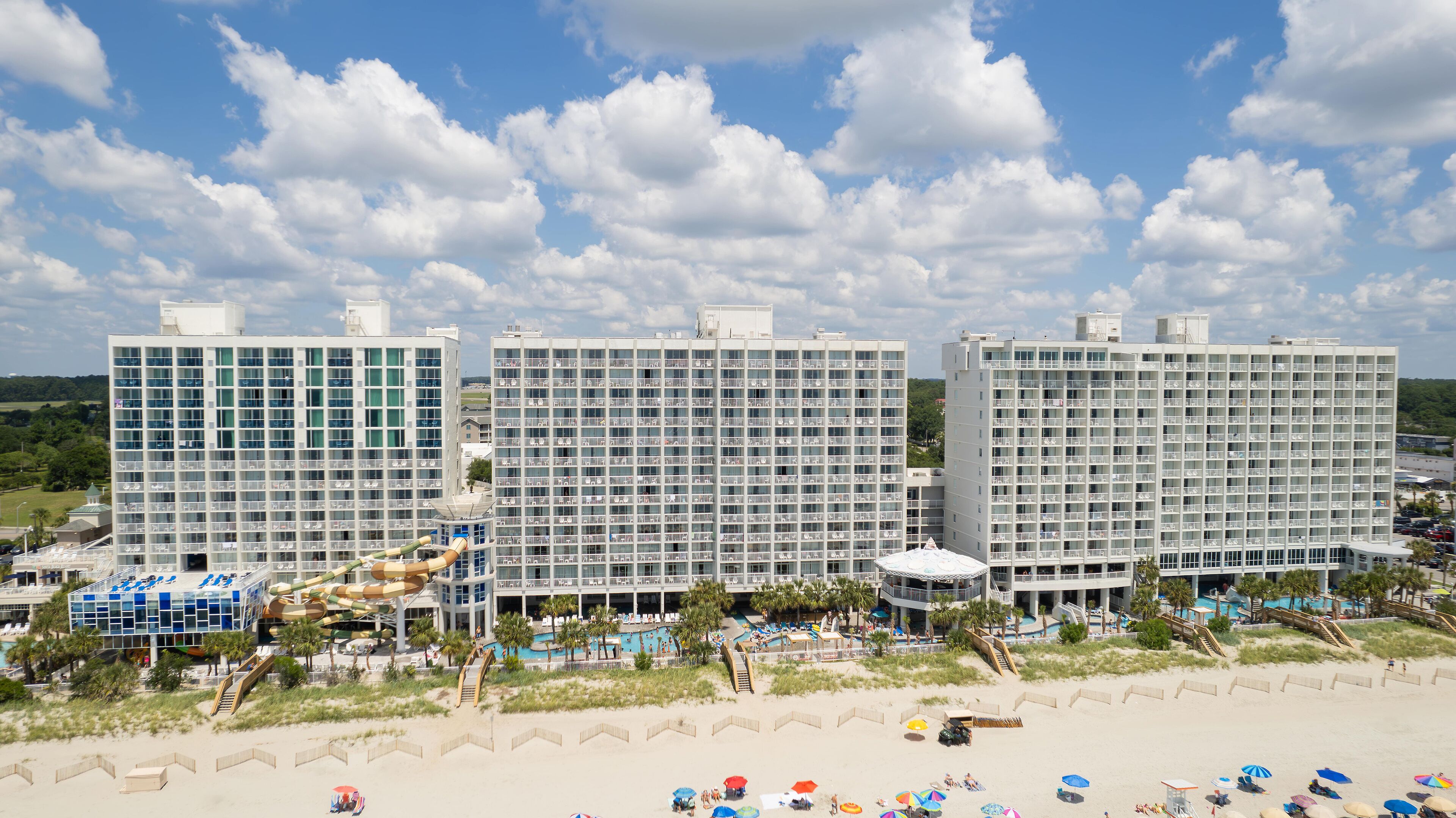 Een strandhotel met meerdere hoge gebouwen, een zwembad en voorzieningen op het strand.