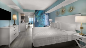 A modern hotel room with a large bed, a desk, a chair, and a view of the kitchen and living area. - Crown Reef Beach Resort and Waterpark (Myrtle Beach)