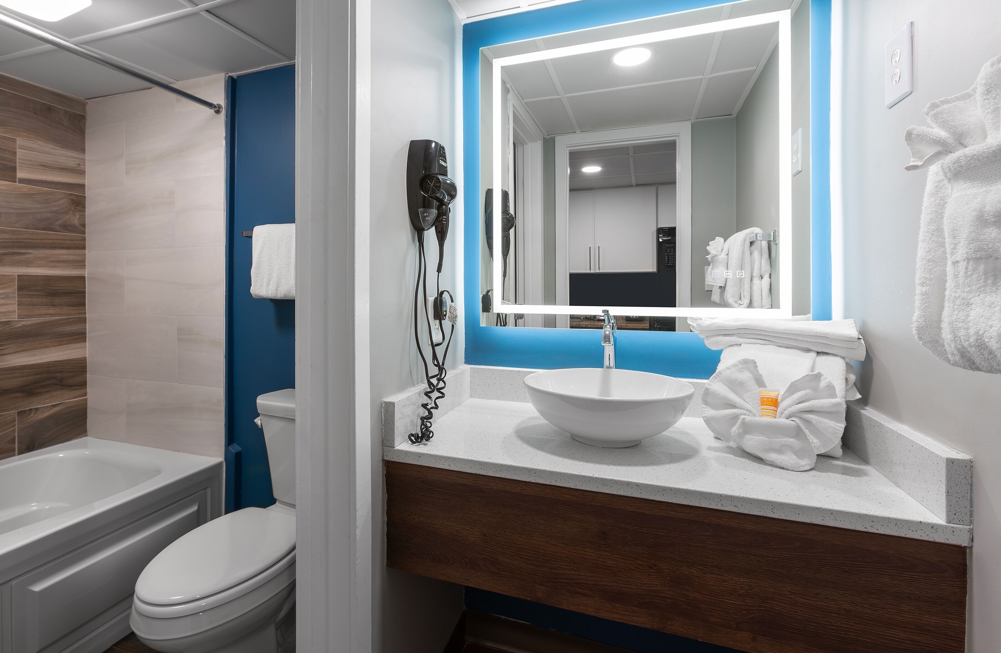 Un baño con un lavamanos blanco, una pared de acento azul, un secador de pelo y un perchero para toallas.