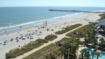 Een strandresort met een zwembad, strandparasols en een pier op de achtergrond.
