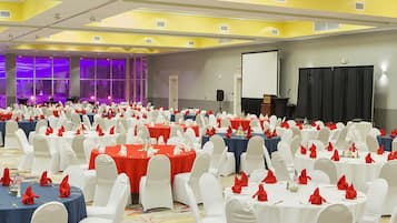 A large conference room with multiple round tables, each with white chairs and red napkins.