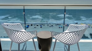 A balcony with two white chairs and a small table, overlooking a beach with people and boats. - Crown Reef Beach Resort and Waterpark (Myrtle Beach)