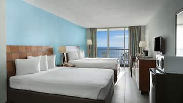 Habitación de hotel con dos camas, televisión, escritorio y vista al océano.