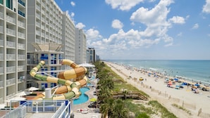 A hotel with a large water slide, a pool, and a beach with umbrellas and people. - Crown Reef Beach Resort and Waterpark (Myrtle Beach)