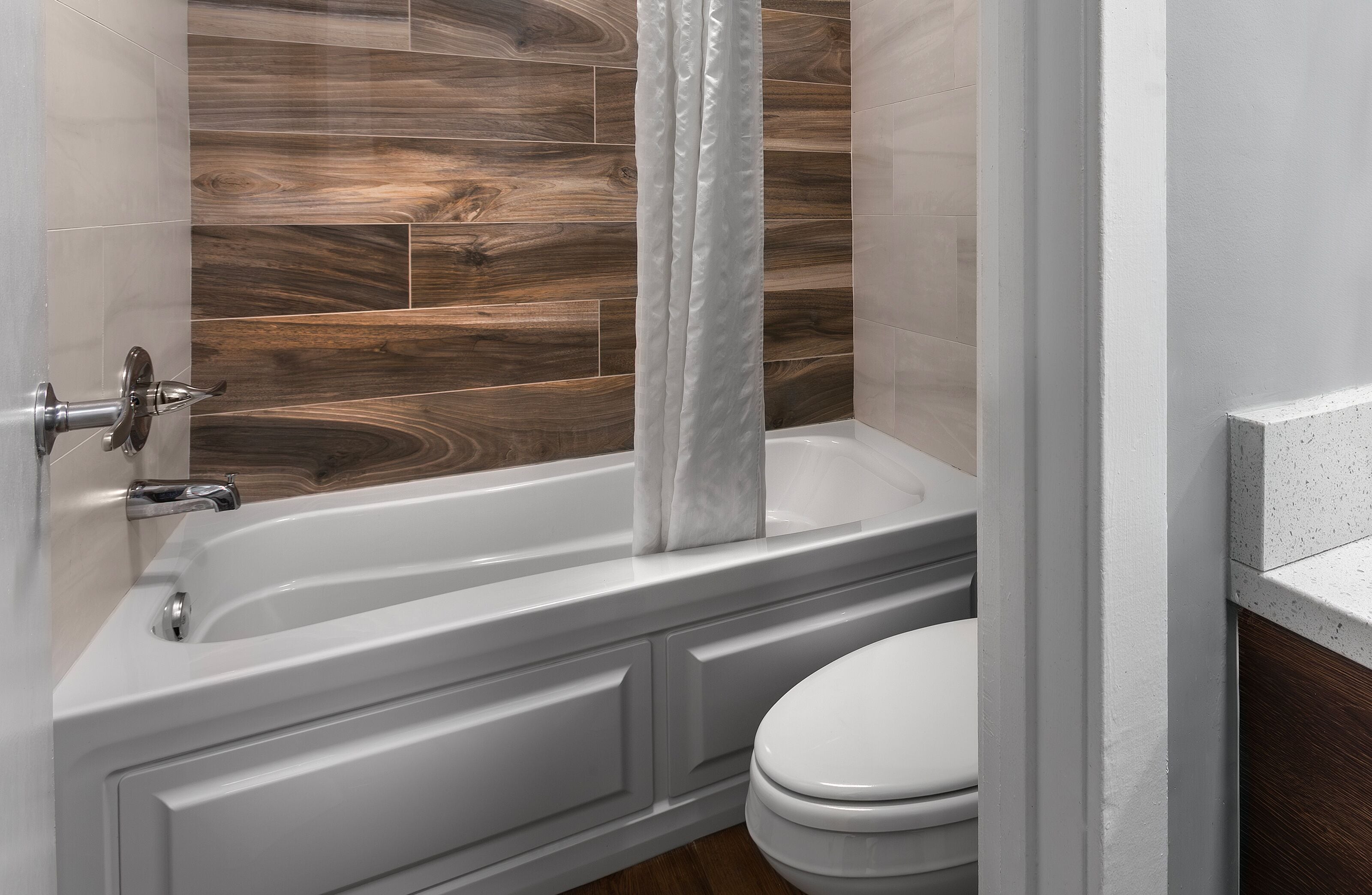 A bathroom with a bathtub, toilet, and wooden wall tiles.