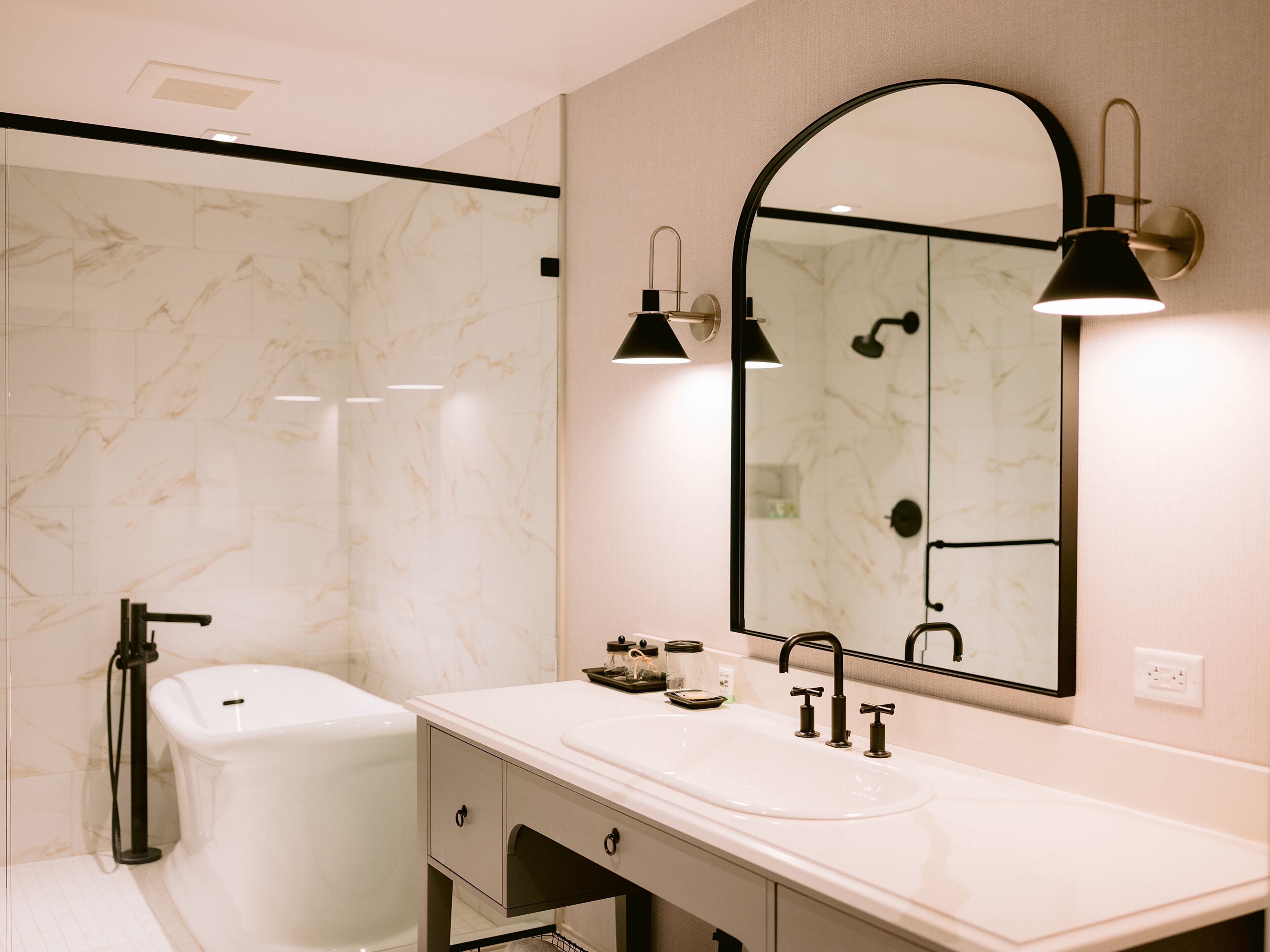 A modern bathroom with a white marble wall, a white sink, a black faucet, and a black handheld showerhead.