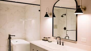 A modern bathroom with a white marble wall, a white sink, a black faucet, and a black handheld showerhead.