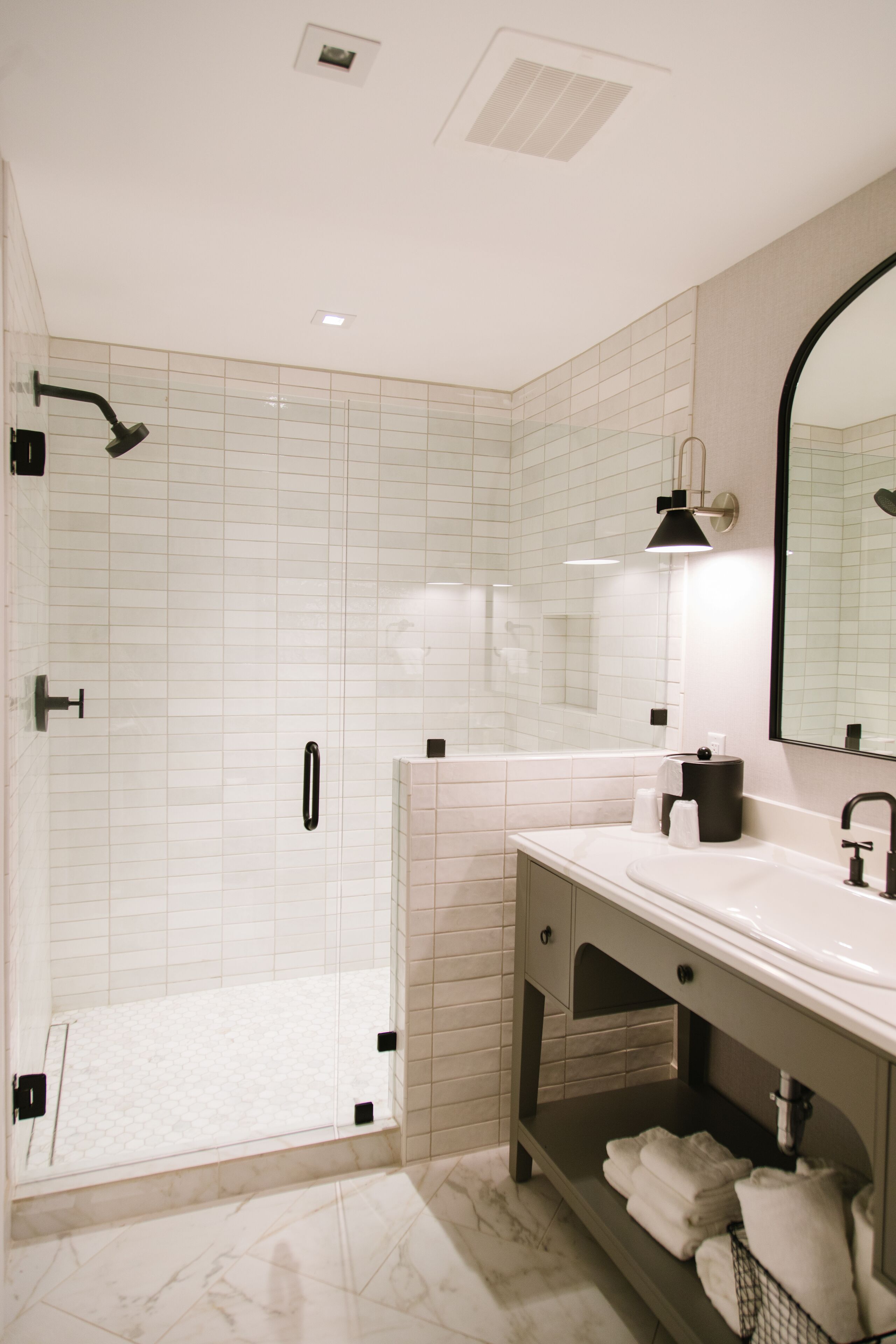 A modern bathroom with a glass-enclosed shower, a vanity with a mirror, and neatly folded towels on a shelf.