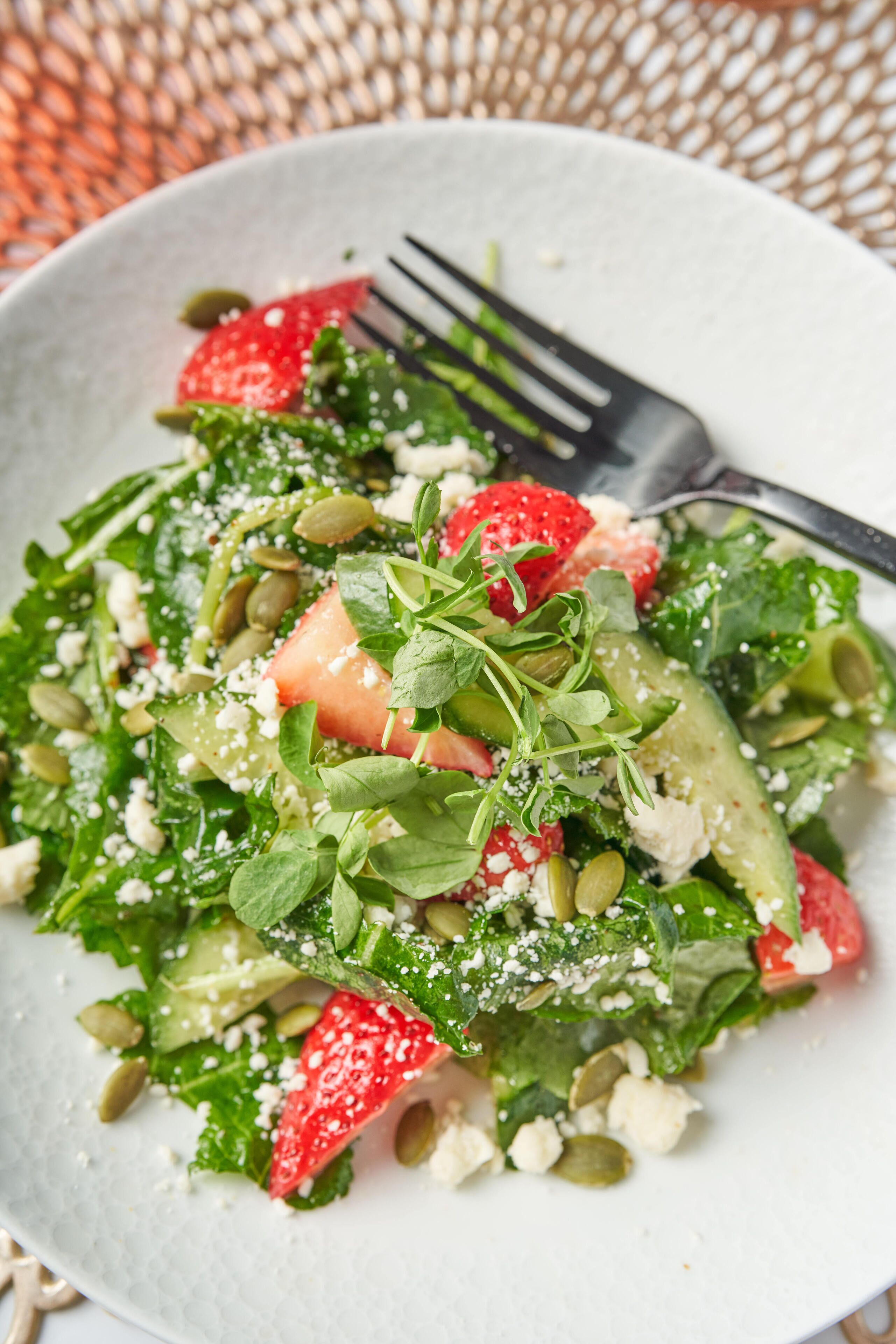 A plate of mixed greens salad with strawberries, pumpkin seeds, and crumbled cheese.