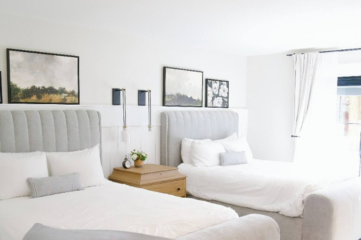 Ein modernes Schlafzimmer mit zwei Betten, einem Nachttisch mit Lampe und gerahmten Bildern an der Wand.