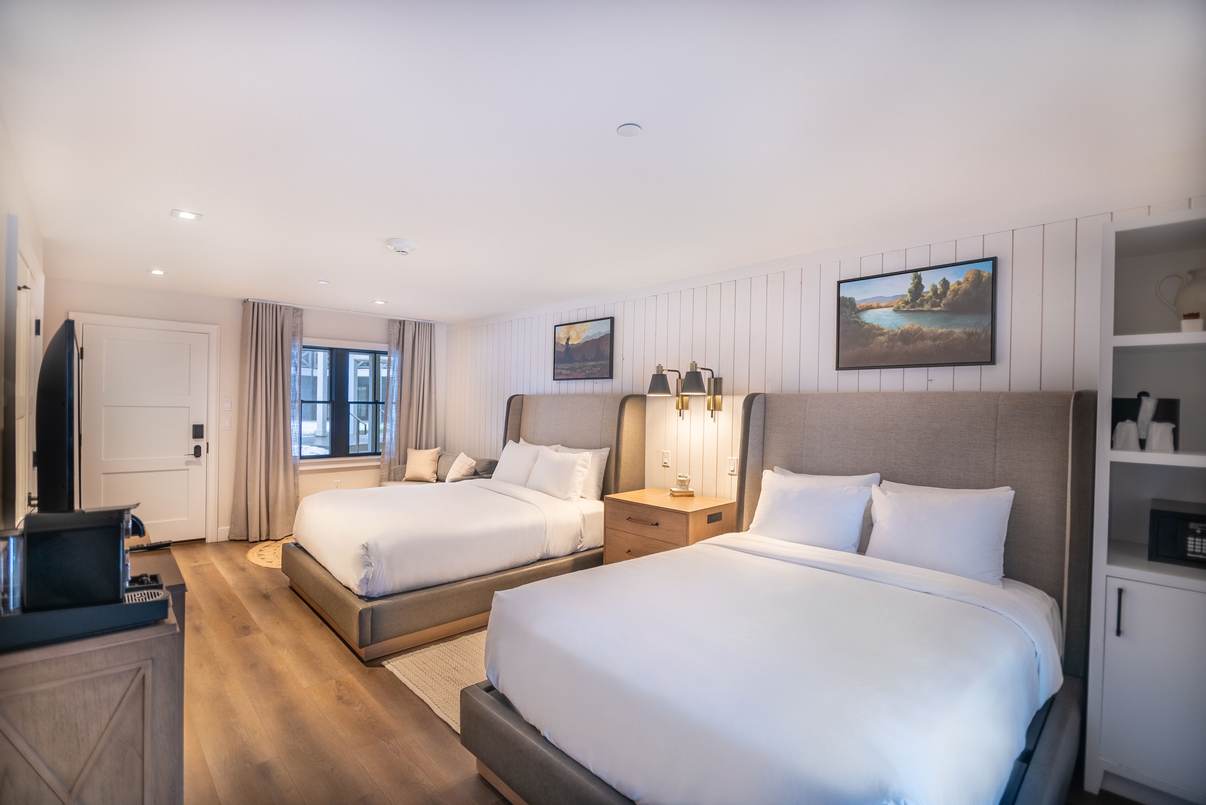 A hotel room with two beds, a desk, a TV, and a bookshelf.