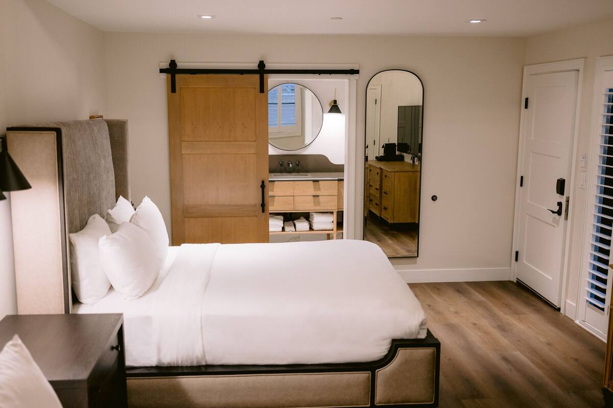 Ein Schlafzimmer mit Bett, Nachttisch, Kommode, Spiegel und einer Schiebetür zum Badezimmer.