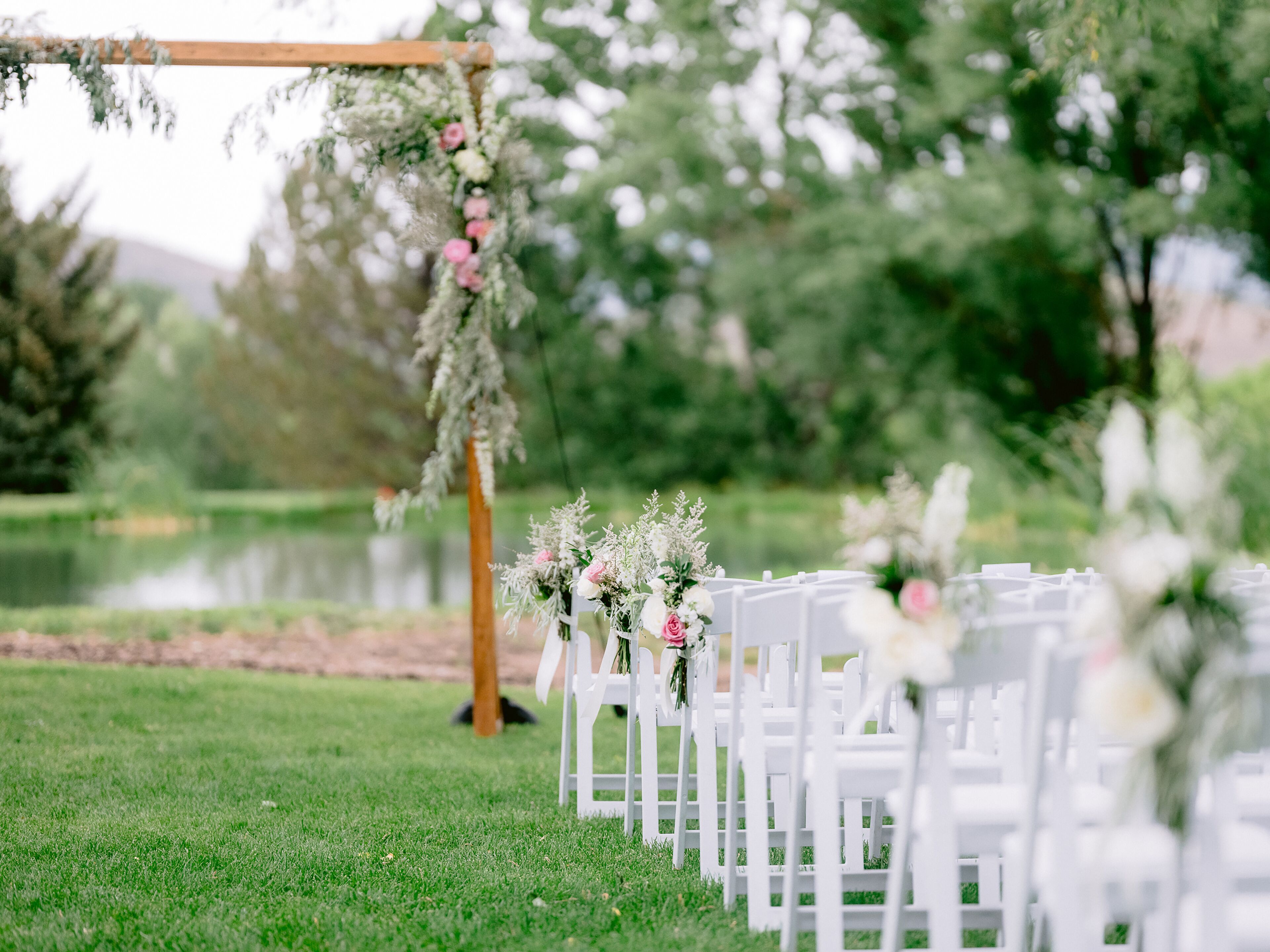 Ein Hochzeitgang mit weißen Stühlen und floralen Dekorationen.