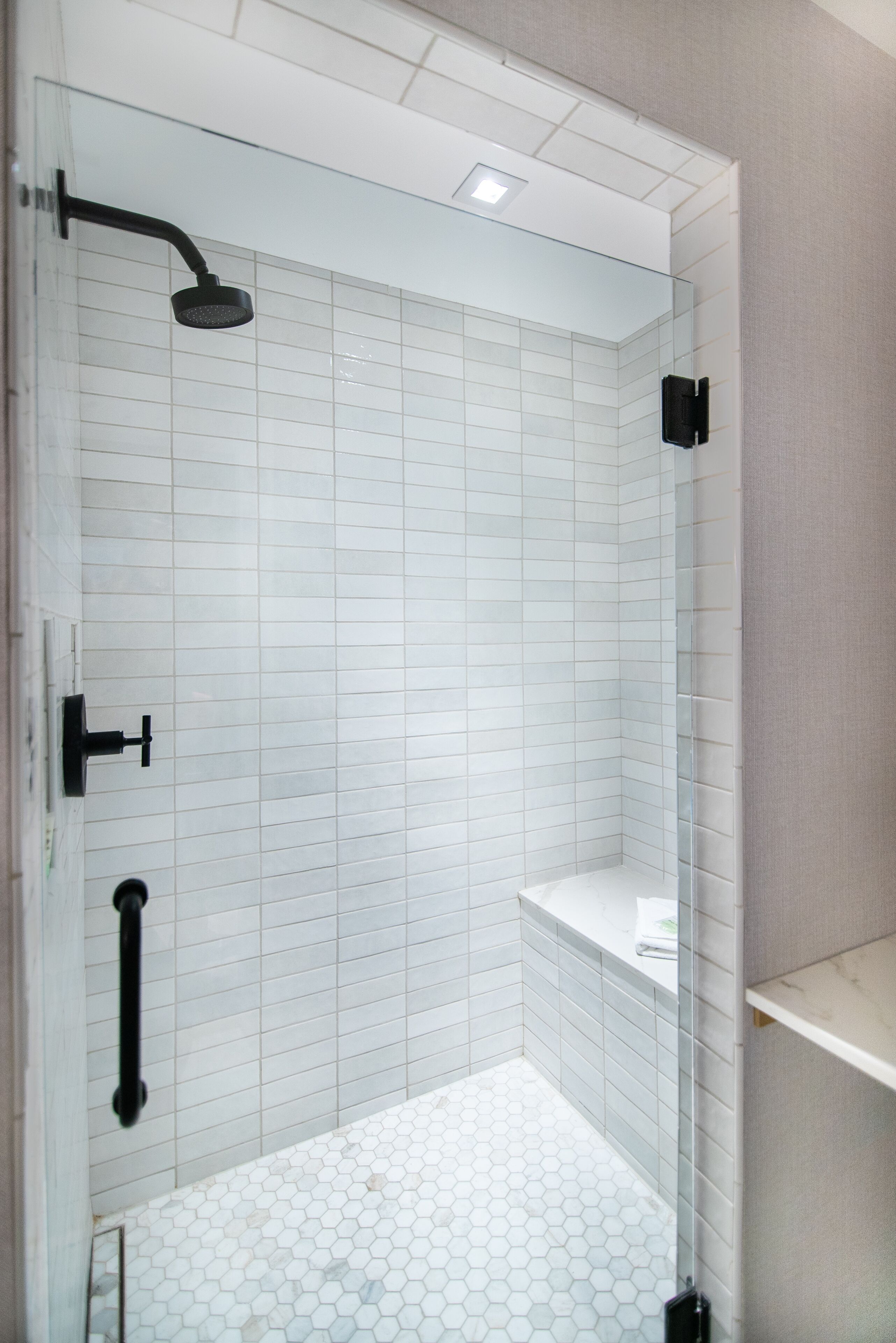 A modern bathroom with white subway tiles, a glass shower enclosure, and a white hexagonal tile floor.