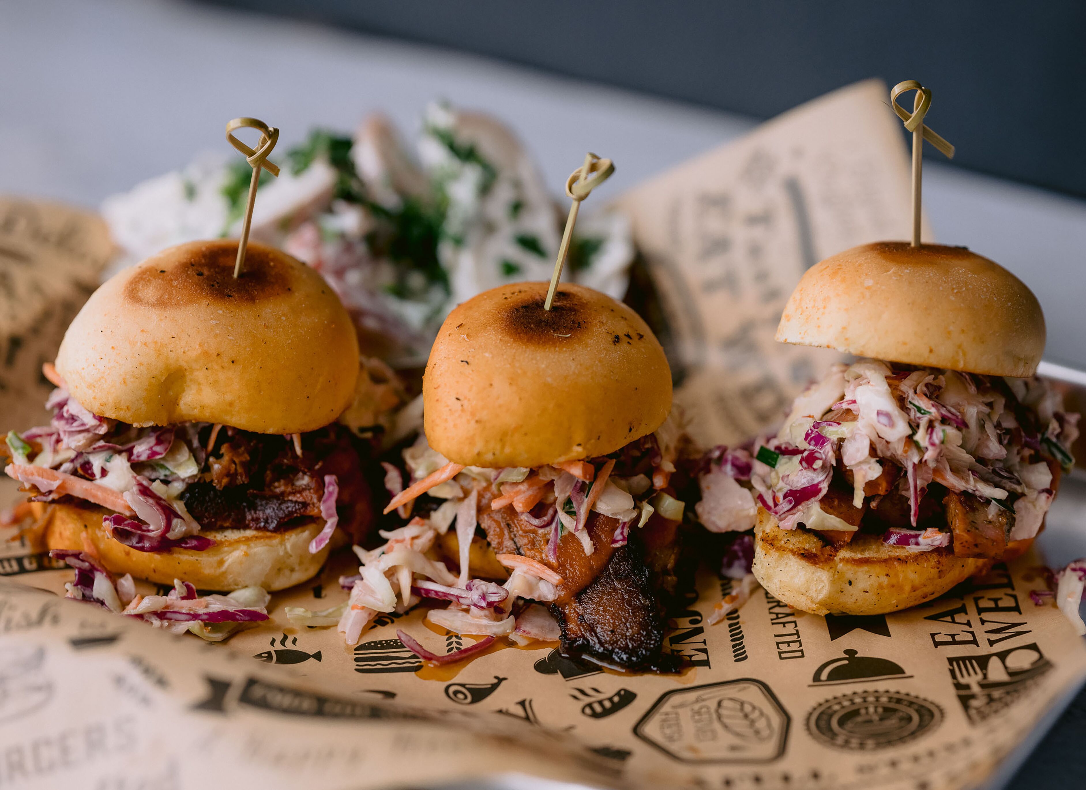 Three sandwiches with toothpicks on a paper with food-related icons.