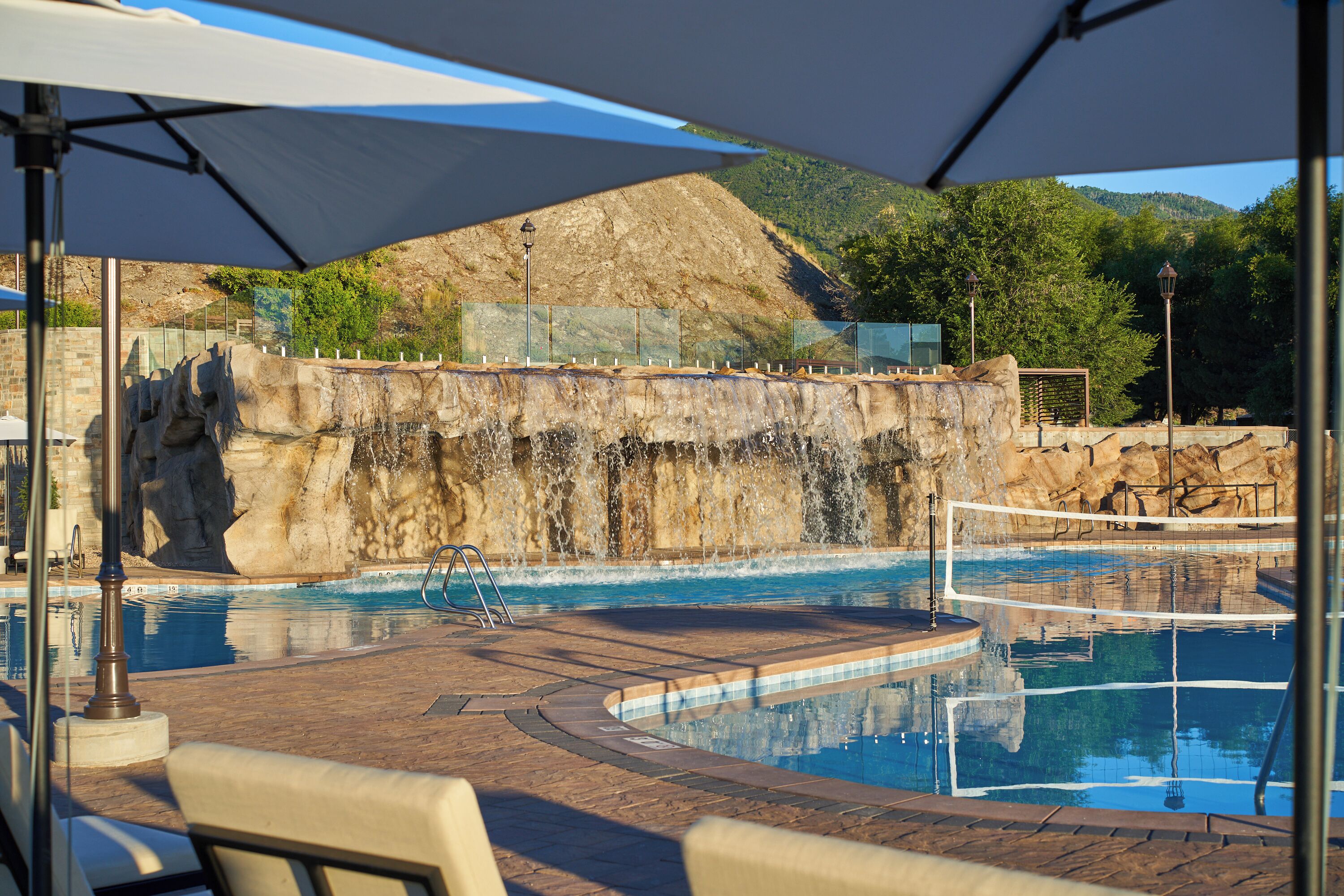 A swimming pool with a rocky backdrop, a lounge area with chairs, and a clear sky.
