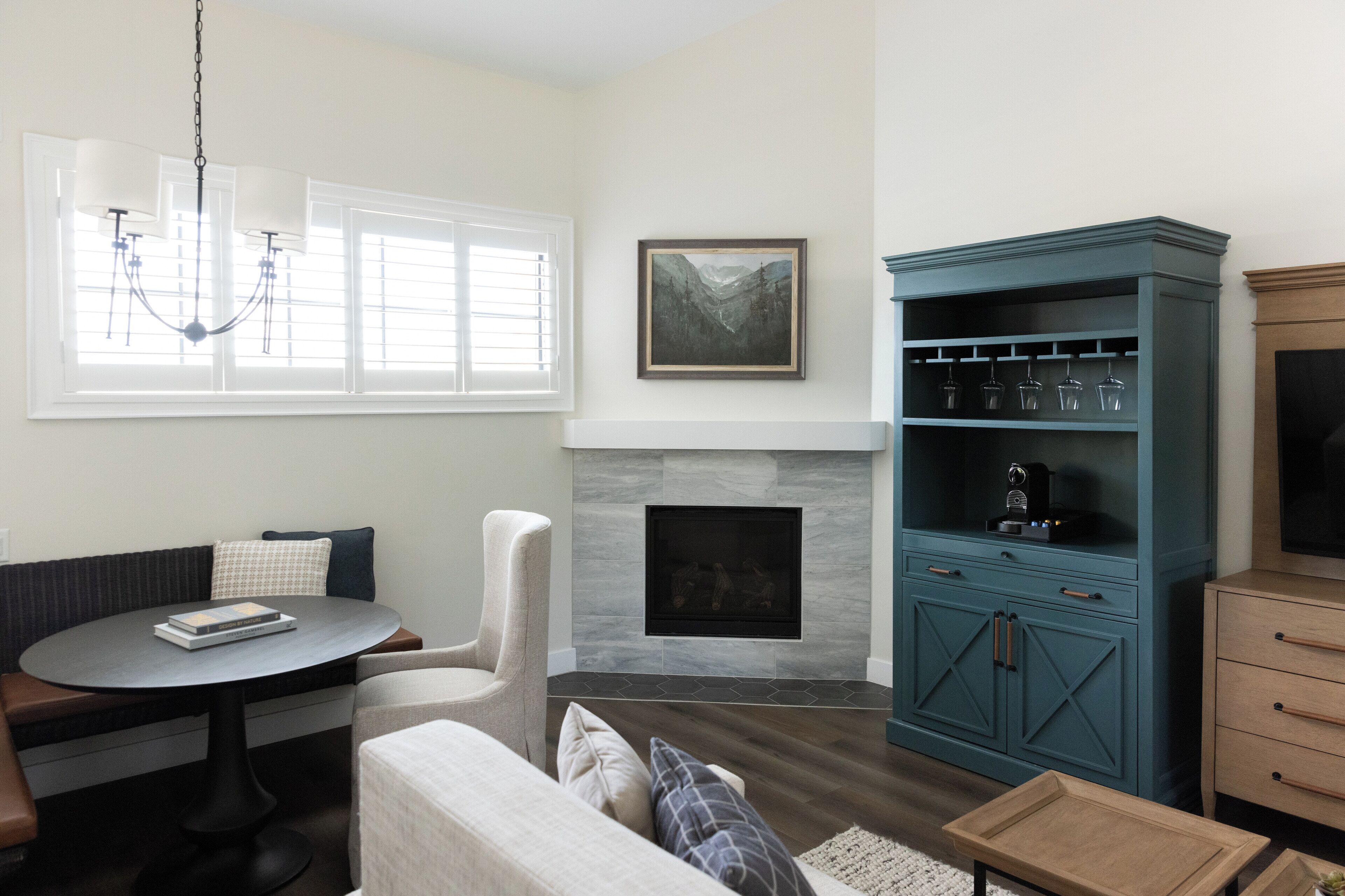 A living room with a fireplace, a blue cabinet with wine glasses, a sofa, a round table, and a chair.