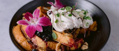 Un plato de postre con panqueques, frutos rojos, crema batida y una orquídea rosa.