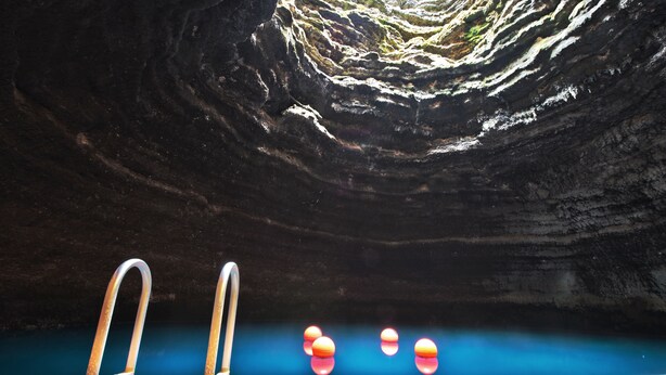 A natural pool with wooden steps and metal ladders, surrounded by a rocky cave wall.