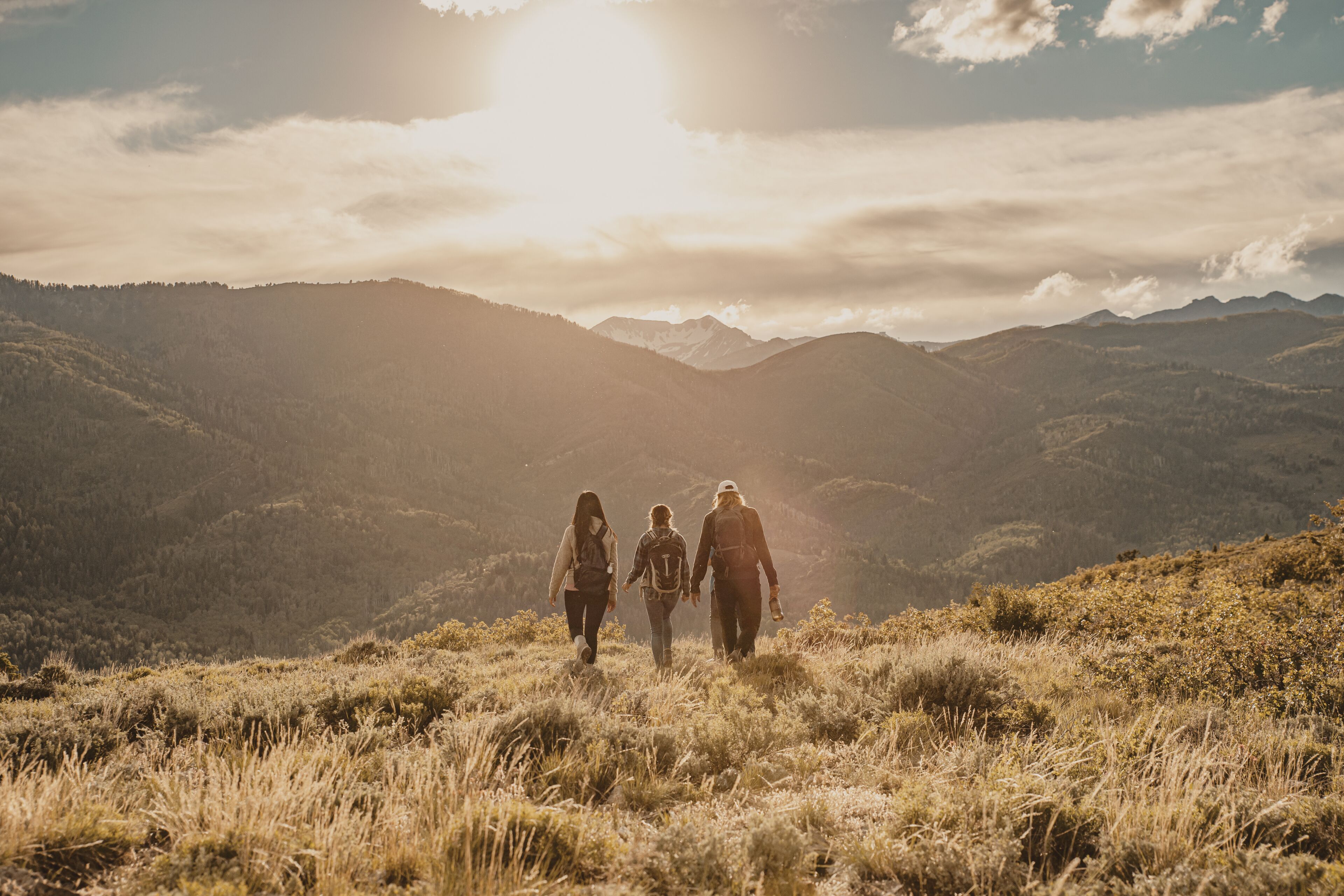 A group of people walking on a grassy hillside with a mountainous landscape in the background.