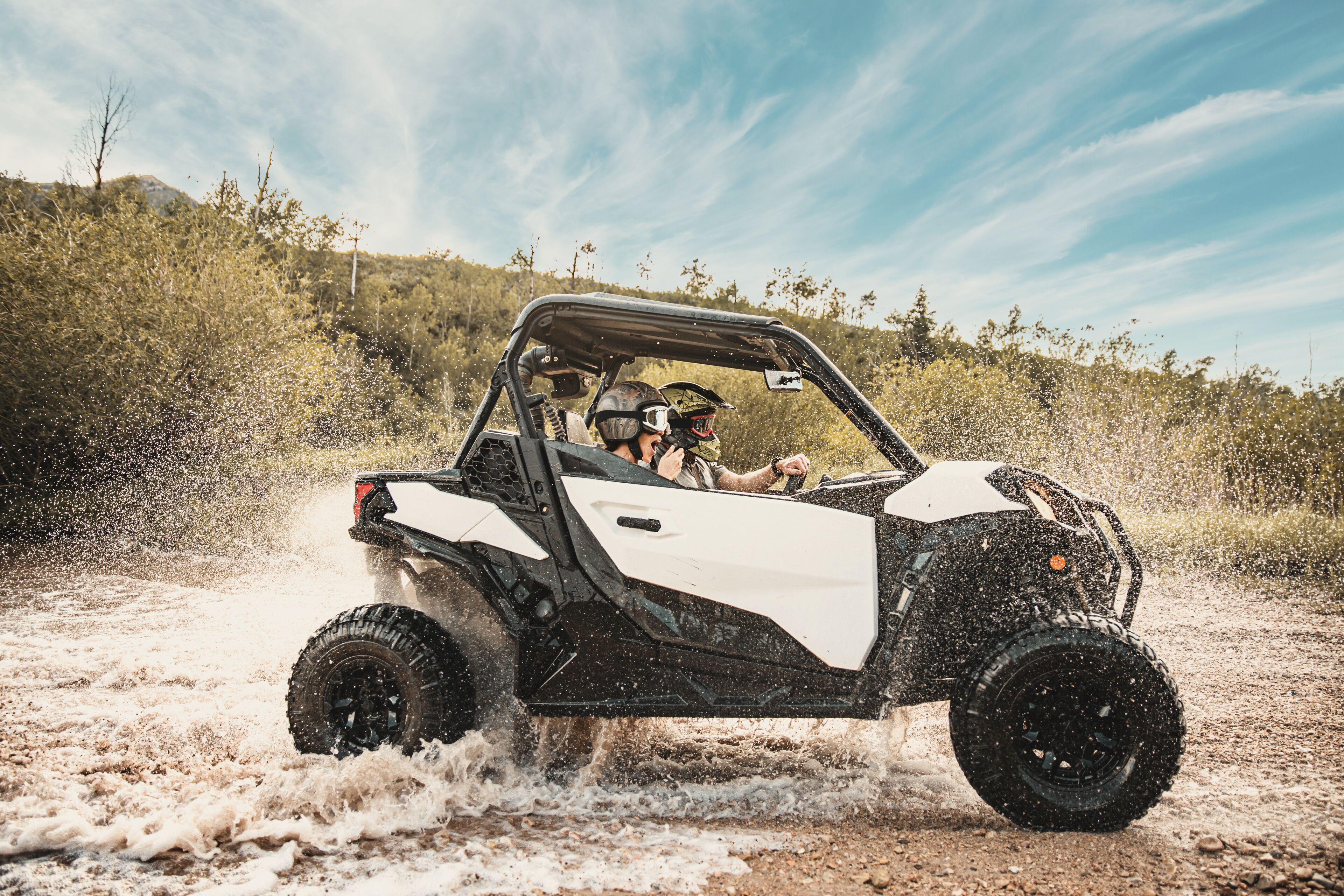 A white and black off-road vehicle driving through a muddy terrain with water splashing around.