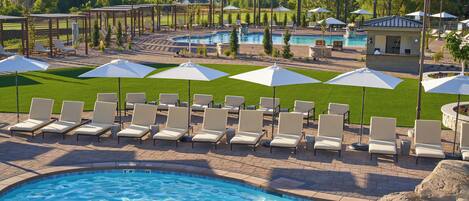 A pool area with lounge chairs and umbrellas, surrounded by a landscaped garden and a view of mountains.