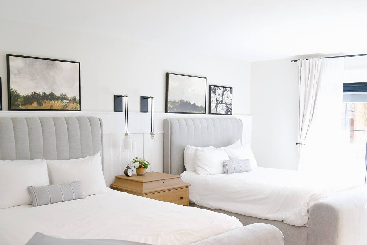 Ein modernes Schlafzimmer mit zwei Betten, einem Nachttisch mit Lampe und gerahmten Kunstwerken an der Wand.