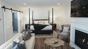 A modern bedroom with a large bed, a sofa, a fireplace, and a TV mounted on the wall.