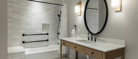 A modern bathroom with a white bathtub, a wooden vanity with a mirror, and a shower area.